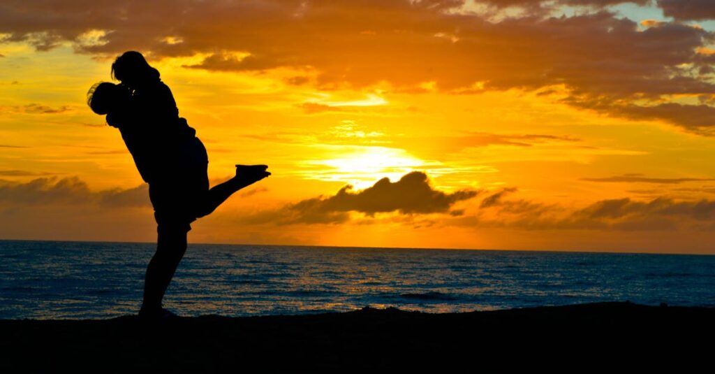 Silhouette of a romantic couple embracing on a beach at sunset, showcasing love and tranquility.
